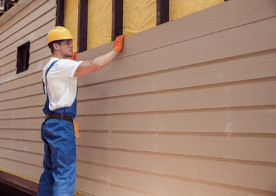 Handsome young man construction worker wearing safety helmet and work overalls while installing wood siding