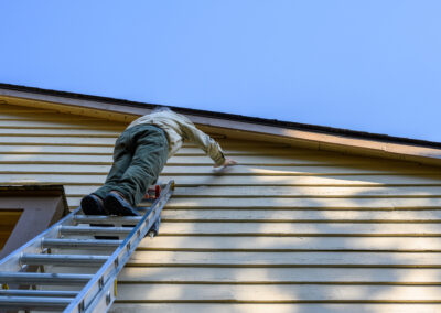 Contractor or worker climbing a silver ladder to inspect or work on the residential siding and roof line.