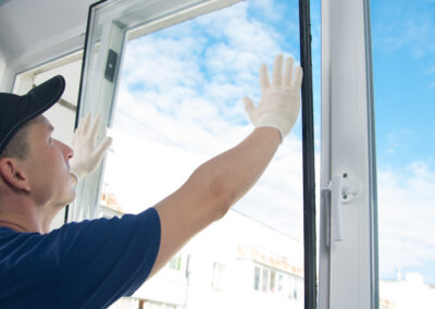 master in protective gloves, changing a double-glazed window in a plastic window, side view, against the blue sky